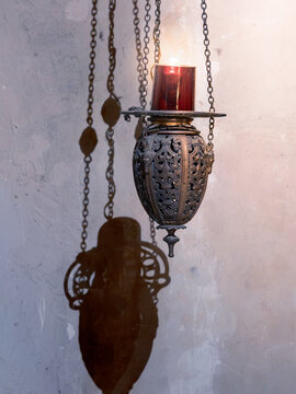 Ancient bronze lamp suspended on chains against wall with sharp shadows
