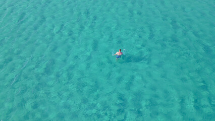 Fototapeta premium Man swimming in clear turquoise waters of Elafonisi beach, Crete, during summer, showcasing vibrant aquatic environment and natural beauty of the Mediterranean region