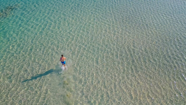 Man swimming in clear turquoise waters of Elafonisi beach, Crete during summer, showcasing the vibrant sea and sandy bottom with gentle waves and sunlight reflections
