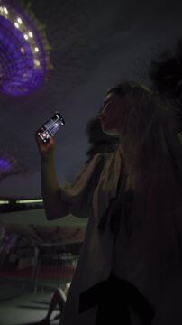 A woman watches a night show at Gardens by the Bay in Singapore. Travel and tourism in Asia, a girl films on her phone.