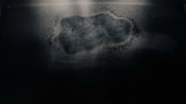 Abstract dark background featuring a textured grainy patch of gray dust particles floating on a smooth matte black surface texture
