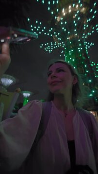 Night city atmosphere at Gardens by the Bay Singapore with tourist filming dazzling light show and illuminated trees during Asian travel