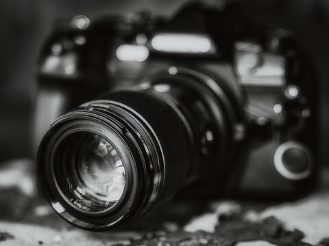 Black and white close up of a modern digital DSLR camera with a large zoom lens and shallow depth of field