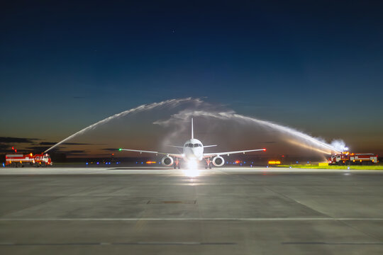 Front view of a white passenger airplane passing through a water arch at night. First visit plane at the airport