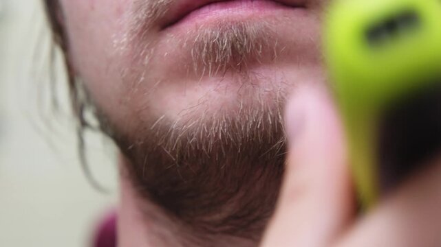 Man trims his beard with a clipper in a bathroom setting at home during the daytime