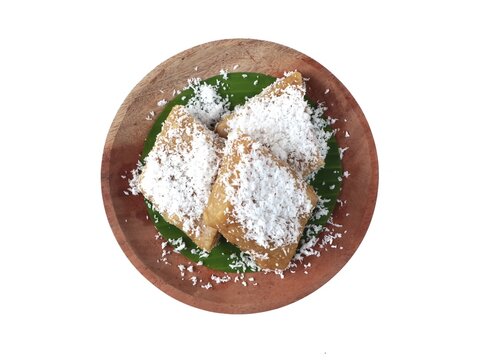 Uli singkong or traditional indonesian steamed cassava cake topped with freshly grated coconut served on a banana leaf and wooden plate, isolated on a white background. Delicious sweet authentic snack