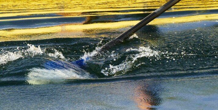 Yellow rowing boat with oar making a splash on the water in high speed motion, on the lake sports activities on the water background
