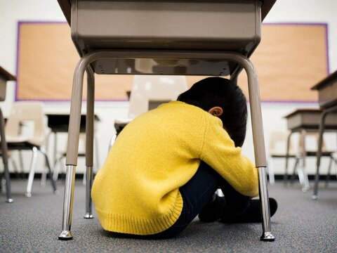 Sad child hiding under a school desk