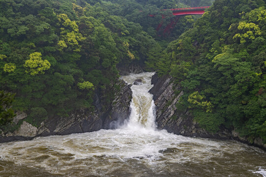the roaring Toroki waterfall plunging into the sea, surrounded by lush green vegetation, and the red bridge over the Taino river