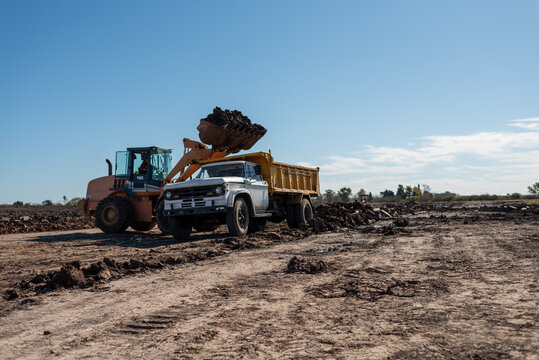 Front loader dumping soil into classic tipper truck at construction site