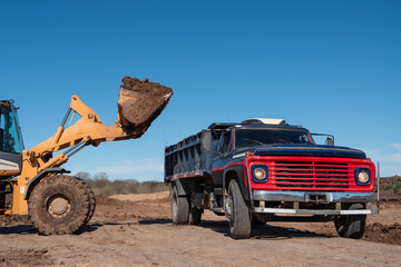 Wheel loader dumping soil into a classic dump truck at construction site © MatiasLeonel