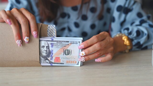 Unidentified woman handles illegal bribery scheme involving paper cash, quietly placing cash inside plain envelope under secret bribery investigation exposing systematic financial bribery.
