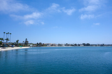 Fototapeta premium Sail Bay landscape with sandy beach shoreline and waterfront vacation rentals and hotels under a partly cloudy sky, San Diego, CA