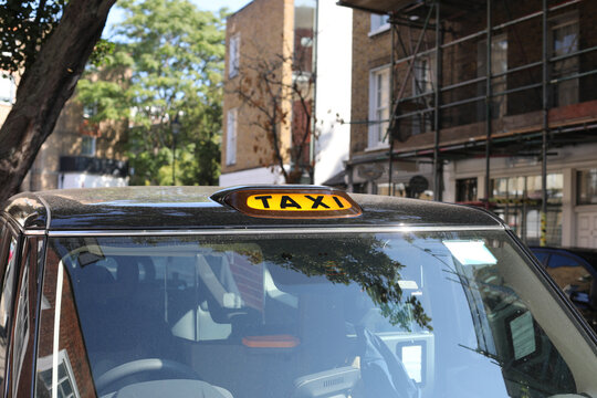 Yellow taxi sign on the roof of a traditional black cab in London street