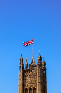 British Union Jack flag flying over the Victoria Tower of the Palace of Westminster in London against a clear blue sky