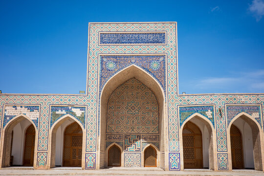 Wide symmetrical view of historic Islamic architecture in Bukhara, Uzbekistan, featuring a monumental pointed arch surrounded by intricate blue and turquoise mosaic tiles, geometric patterns