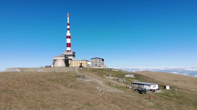 Aerial view of Botev Peak with its prominent telecommunications tower and mountain station buildings on the grassy summit under a clear blue sky in Lovech, Bulgaria.