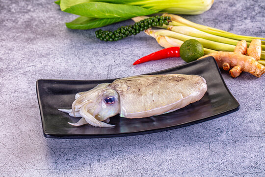 Raw cuttlefish on black plate with lemongrass, lime, chili, and ginger background