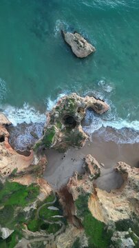 Aerial view of the dramatic rock formations and turquoise waters at Praia dos Tres Irmaos along the coastline in Alvor, Faro, Portugal.