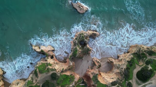 Aerial view of Praia dos Tres Irmaos with turquoise waves crashing against golden rock formations and sandy beaches in Alvor, Faro, Portugal.
