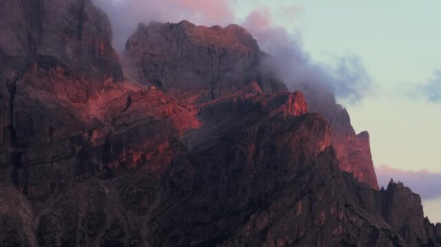 Aerial view of the rugged Dolomites peaks illuminated by golden light with clouds drifting around the rocky slopes in Primiero San Martino di Castrozza, Trentino-Alto Adige, Italy.