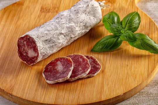 Traditional dry cured salami with slices and fresh basil garnish on a wood platter
