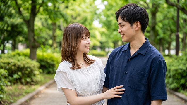 Happy young Japanese couple walking together in a lush green park on a warm spring day, sharing romantic moments and smiling at each other