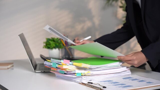 Businesswoman hands working in Stacks of paper files for searching and checking unfinished document achieves on folders papers at busy work desk office.	