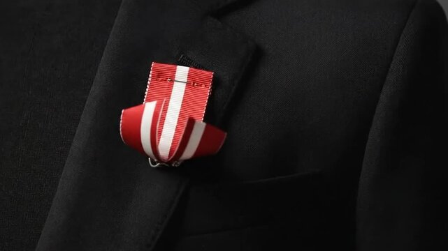 Red and white striped fabric ribbon badge pinned to a black blazer suit