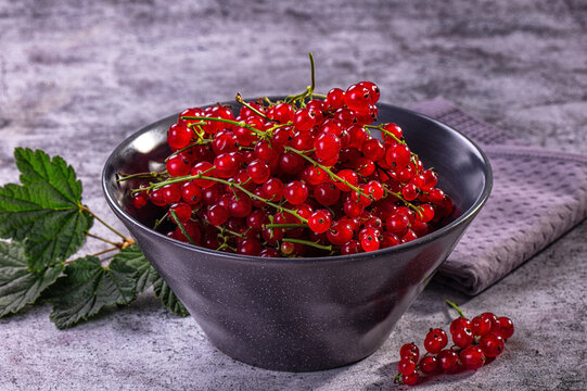 Fresh red currants in black bowl with green leaves on textured gray surface