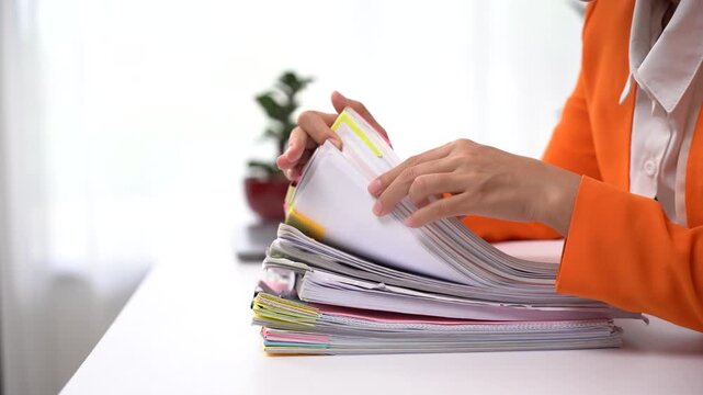 Businesswoman hands working in Stacks of paper files for searching and checking unfinished document achieves on folders papers at busy work desk office.	