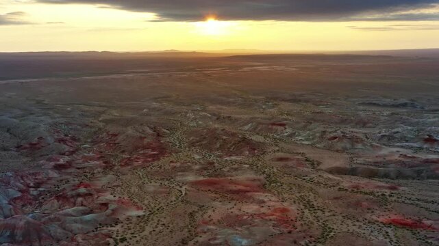 Aerial view of the Tsagaan Suvarga rock formations at sunset, featuring colorful sedimentary layers and vast desert landscape in O'lziit, Dundgovi, Mongolia.