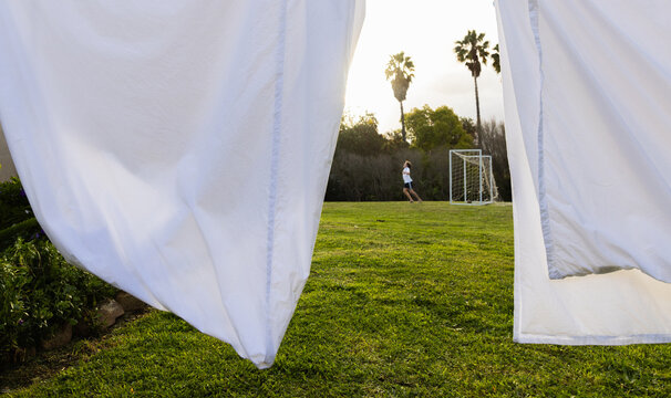 teenage soccer player visible through white sheets drying on clothes line at sunset