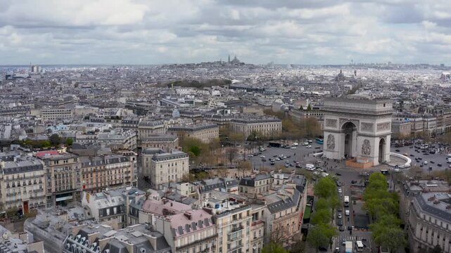 Aerial view of the iconic Arc de Triomphe surrounded by historic Parisian buildings and streets under a cloudy sky in Paris, Ile-de-France, France.