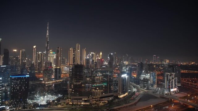 Illuminated skyscrapers and Burj Khalifa rise over Dubai Canal with highway traffic flowing through the city at night