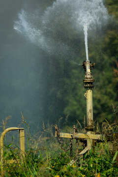 Close-up of an irrigation sprinkler head spraying water with metal chains and farm hardware visible, Gers, Saint Georges, France