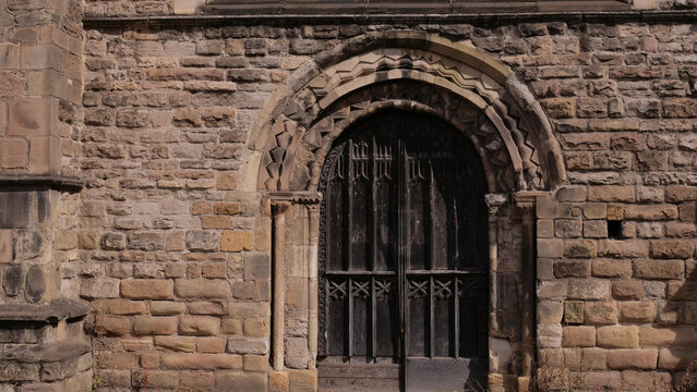 Ancient medieval stone church portal with dark ornate wooden door and carved stone archway architecture