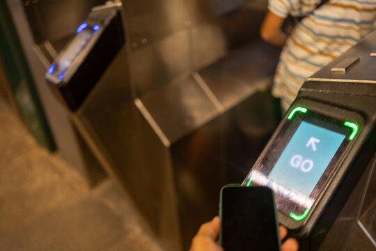 Hand using a smartphone for contactless payment at a subway turnstile, showing digital transaction technology for public transit access and modern urban commuting