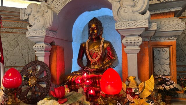 Horizontal close up view of a seated Buddha statue on a temple altar with lotus lamps and Dharmachakra wheel