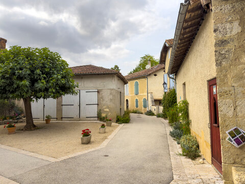 Quiet lane lined with stone houses and white barn doors in the village center, Gers, Sarrant, France