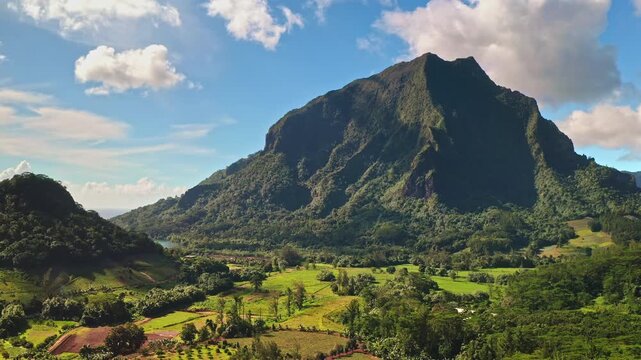 French Polynesia, Moorea island vibrant green tropical landscape, prominent volcanic mountain, lush valleys, agricultural fields, and beautiful blue bay under bright sky. Rise up aerial drone panorama
