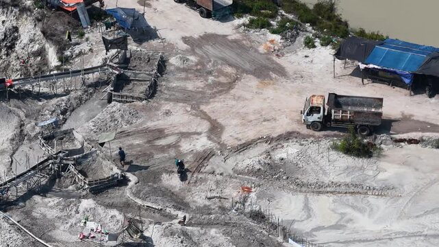 Industrial mining site with heavy trucks and workers processing sand on a sunny day in Indonesia