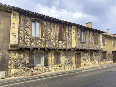 Half-timbered stone house with shuttered windows along a village street, Gers, Pavie, France