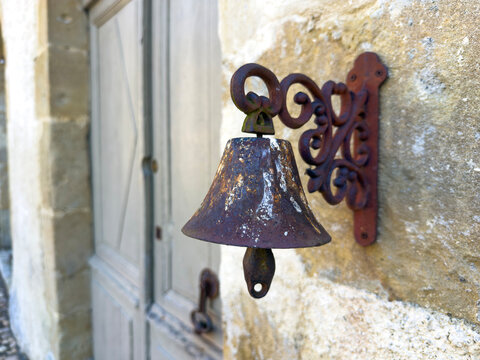Antique iron bell mounted beside a wooden door on a stone wall, Gers, Montesquiou, France