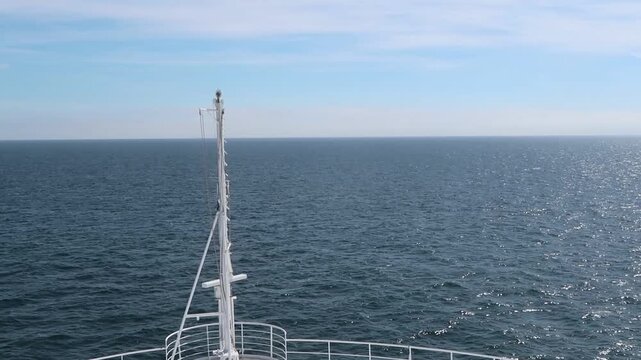 Bow of a white cruise ship sailing across the calm deep blue sea towards the horizon and cloudy sky. Travel freedom and adventure. Bright summer day outdoors