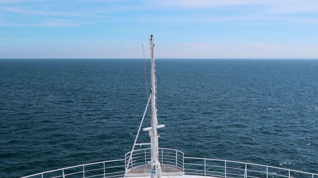 Bow of a white cruise ship sailing across the calm deep blue sea towards the horizon and cloudy sky. Travel freedom and adventure. Bright summer day outdoors