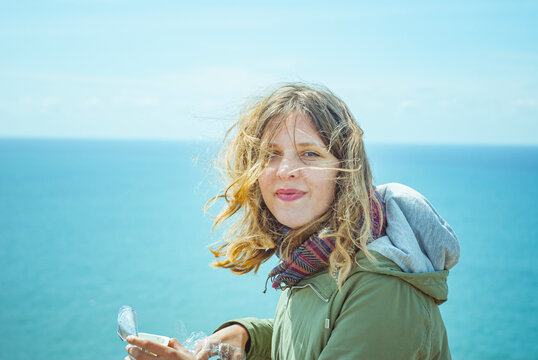 Young woman with windblown hair holding a container with ocean background
