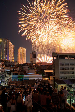 Bangkok, Thailand - 31 December 2025: View of New Year firework at Iconsiam illuminating the night sky above the urban skyline with a crowd of people watching from a rooftop terrace.