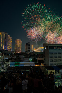 Bangkok, Thailand - 31 December 2025: View of New Year firework at Iconsiam illuminating the night sky above the city skyline with a crowd of people watching from a rooftop.