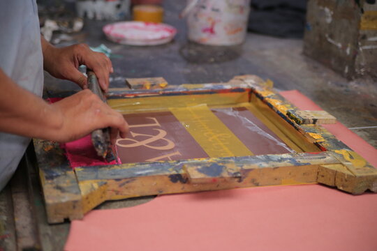 Lahore, Pakistan - 02 October 2024: View of a worker using a wooden screen printing frame to apply pink ink onto a surface at the Quaid-e-Azam Industrial Estate.